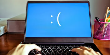 laptop with hands typing blue screen with frown face