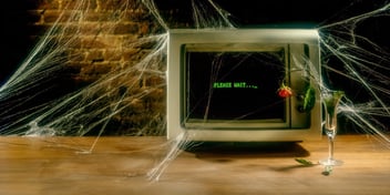 old outdated computer with the text, please wait, on screen on a desk with cobwebs and dying flowers on it 