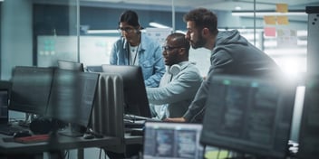 managed IT department working in office team gathered around one computer looking at the screen